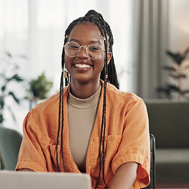 Woman with glasses smiling while working on laptop