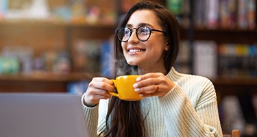 Woman with glasses smiling while drinking coffee