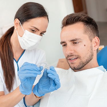 Dentist with white mask showing patient a set of clear aligners